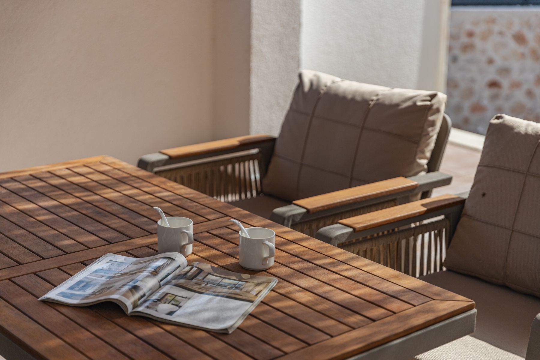 An outdoor table in dappled sunlight with two cups of coffee and open papers